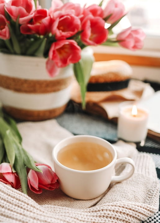 Cup of tea, pink tulips and a lit candle on a knitted blanket