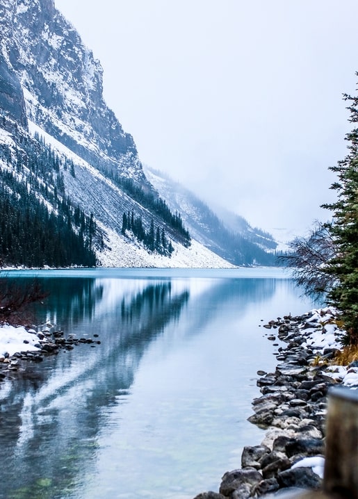 Turquoise mountain lake with snow-capped peaks and pine forest in winter mist
