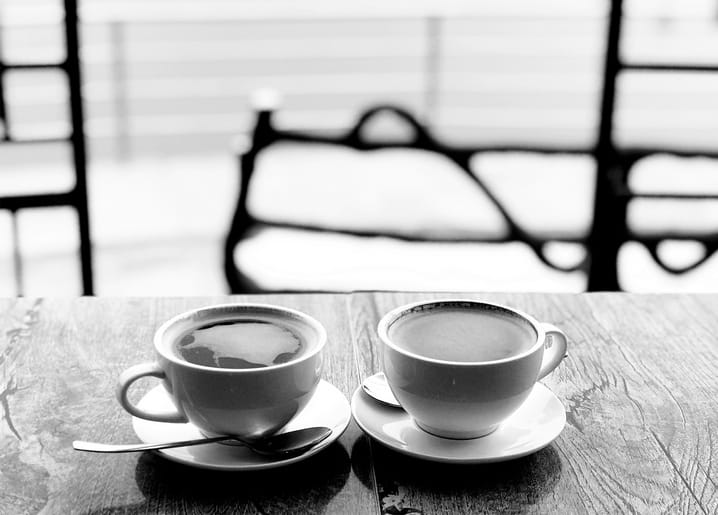 Zwei Kaffeetassen mit Untertassen und Löffel auf einem hölzernen Cafétisch