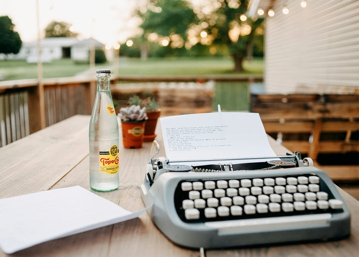 Vintage typewriter, water bottle and string lights on a wooden veranda table