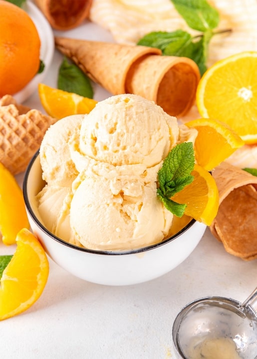 Vanille-Orangen-Eis in weißer Schale mit Orangenscheiben und Waffeltüten