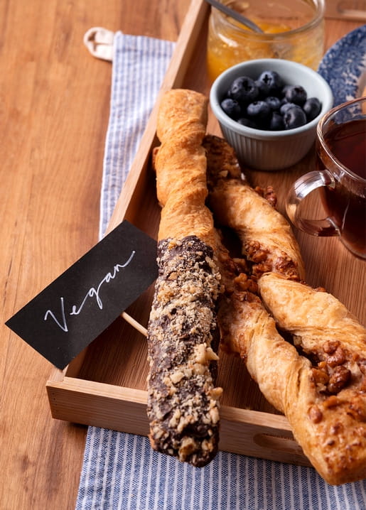 Vegan chocolate-walnut and caramel-walnut pastry twists on a wooden tray with tea, jam and blueberries