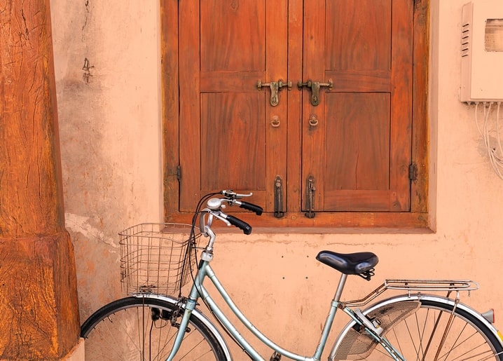Vintage bicycle parked against a terracotta wall beneath weathered wooden window shutters