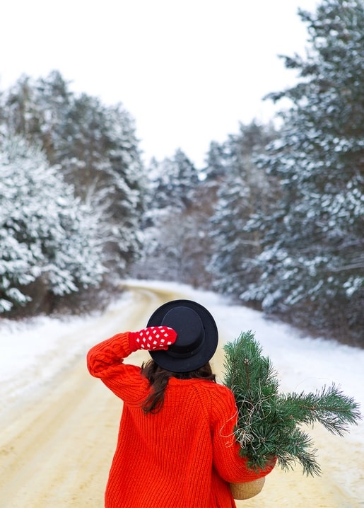 Woman in a red sweater and black hat walking a snowy forest road with fir branches