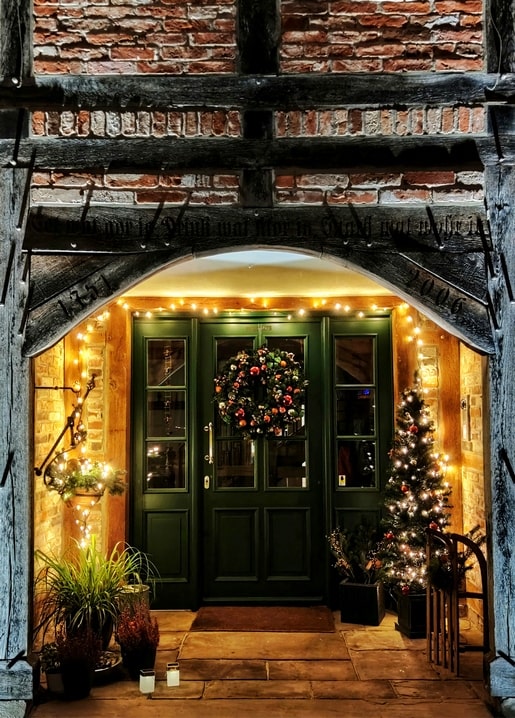 Green door under a brick archway decorated with a wreath and Christmas lights