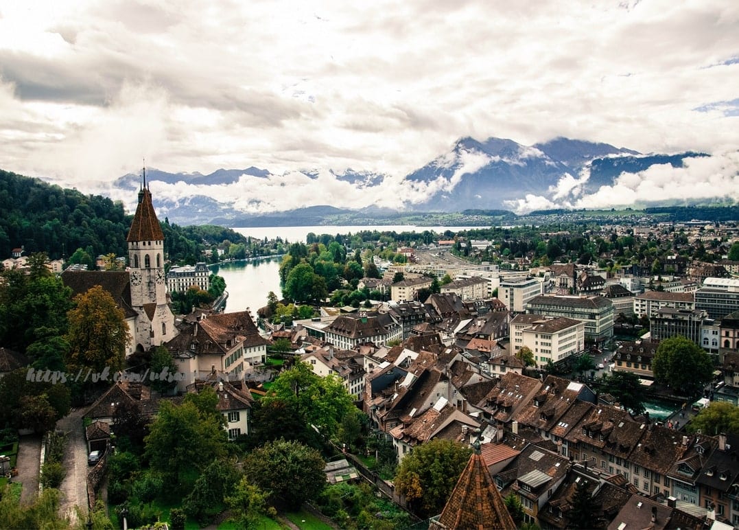 Schweizer Altstadt mit Kirchturm, See und wolkenverhangenen Alpen aus der Vogelperspektive