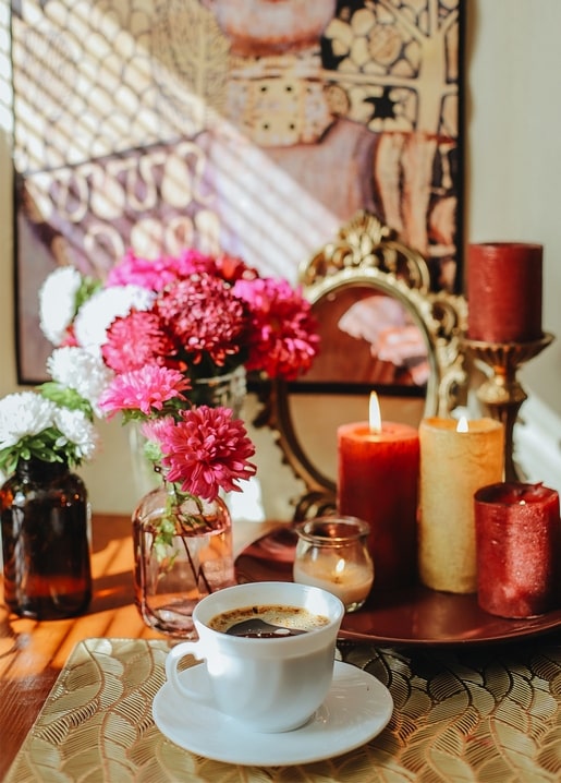 Cup of coffee with pink chrysanthemums and lit candles on an autumn table