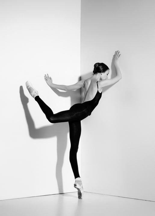 Schwarzweißfoto einer Ballerina in scharfer Eckpose mit hoch erhobenem Bein