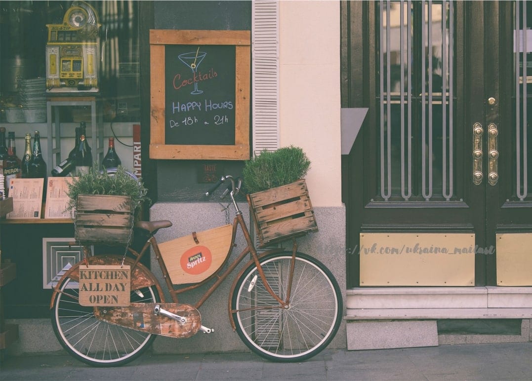 Old bicycle with wooden herb crates parked outside a French café with a chalkboard cocktail menu