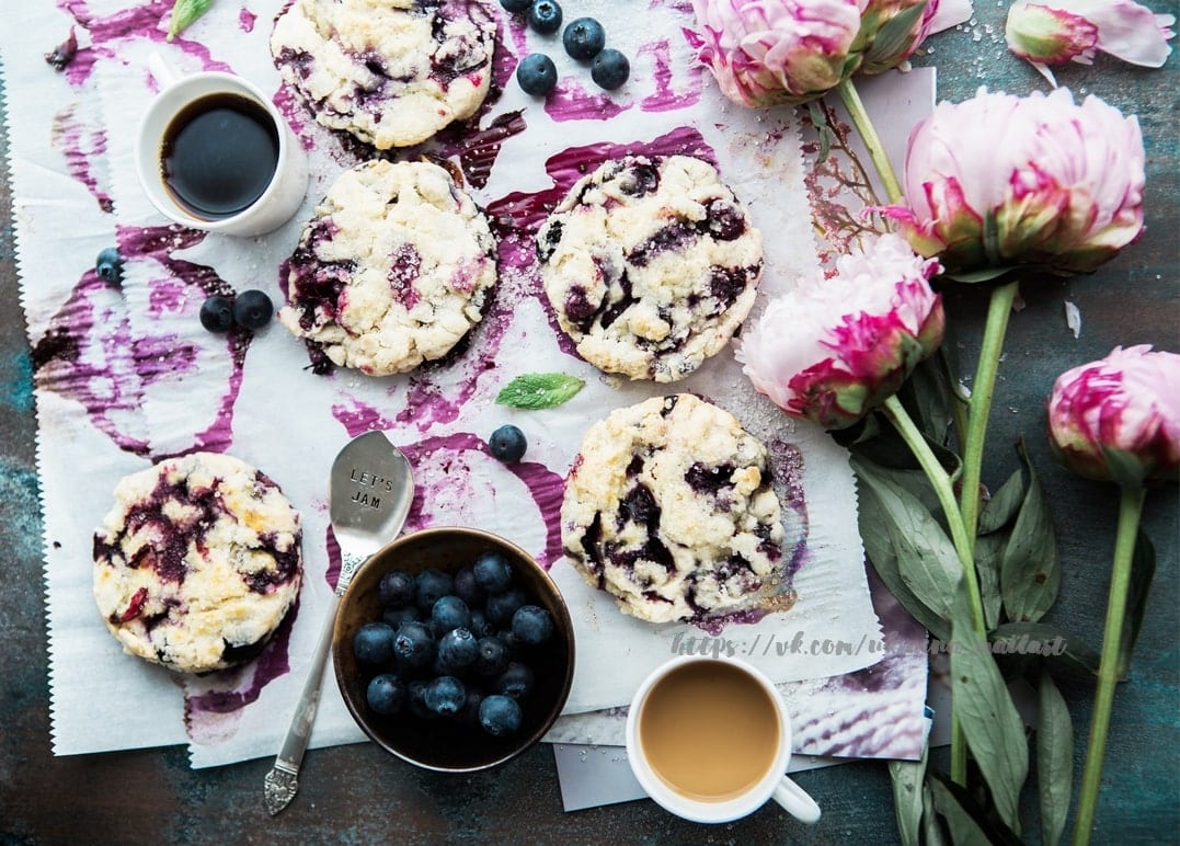 Blaubeer-Scones, Kaffeetassen und rosa Pfingstrosen auf einem beerenverfärbten Tisch