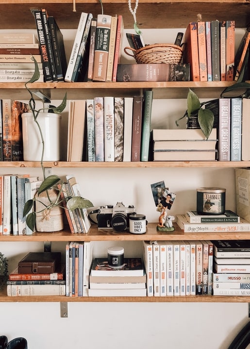 Дерев'яна книжкова полиця з приглушеними книгами, рослинами, фотоапаратом і кухлем «Good Vibes Only»