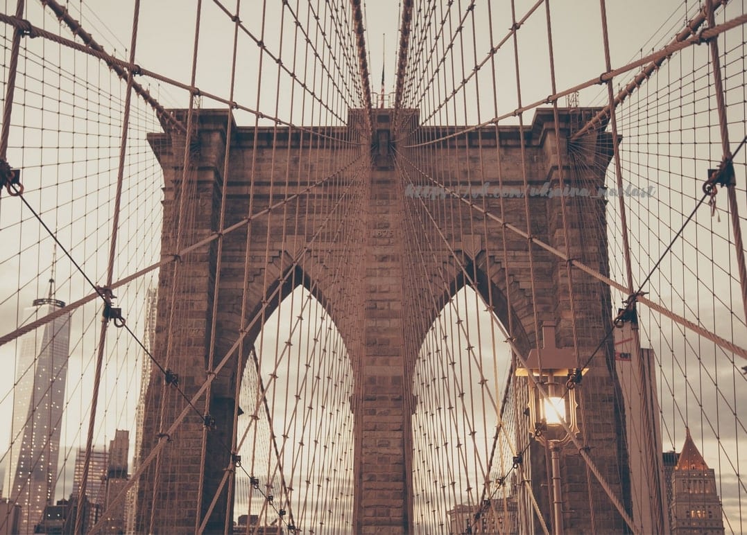 Steinturm und Kabel der Brooklyn Bridge vor der Skyline Manhattans in der Dämmerung
