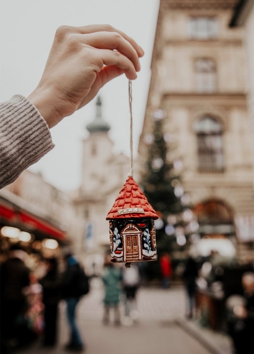 Hand hält einen Keramikanhänger mit rotem Dach über einem Weihnachtsmarkt