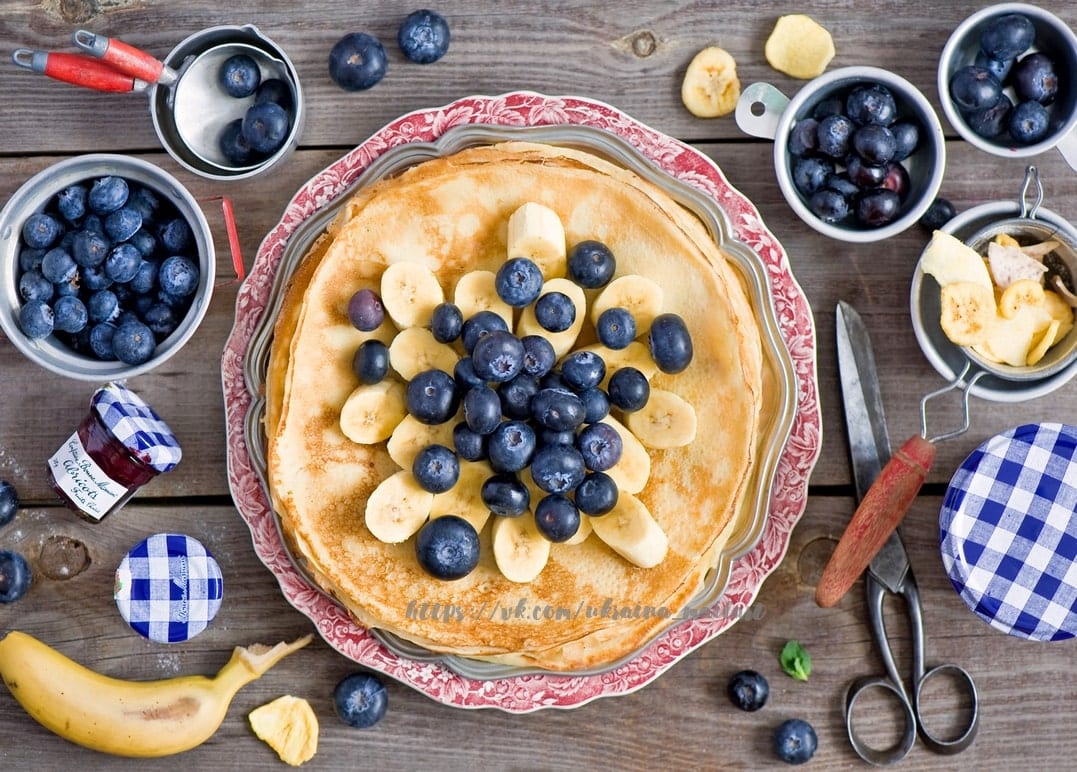 Stapel Pfannkuchen mit Heidelbeeren und Banane auf einem floralen Vintage-Teller