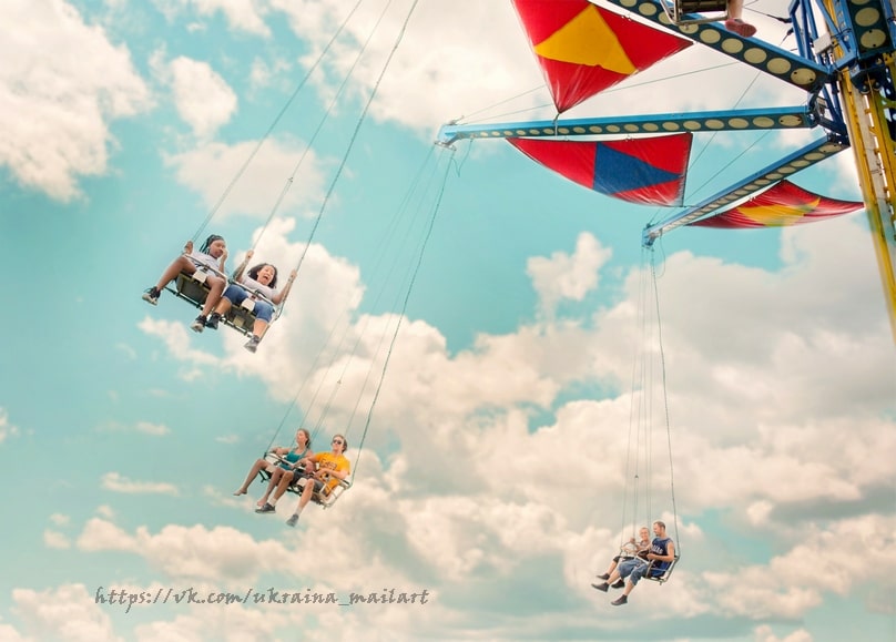Chain swing fairground ride soaring above clouds against a blue sky