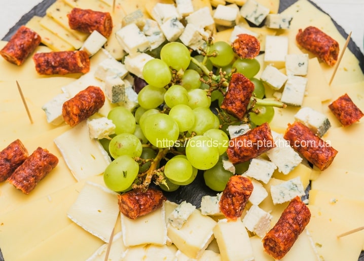 Cheese platter with brie, blue cheese, grapes and chorizo bites on slate