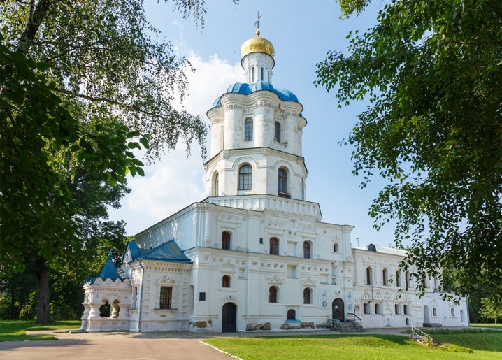 White bell tower with blue cupolas and a gold dome surrounded by green trees in Chernihiv