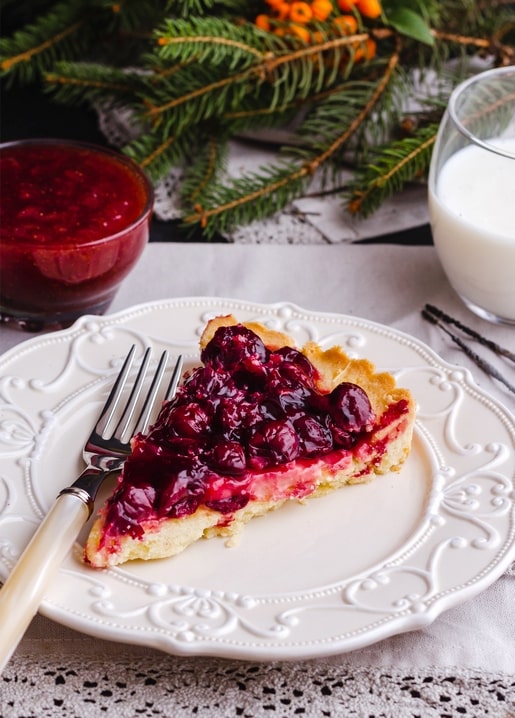Stück Kirschkuchen auf verziertem Teller mit Preiselbeersauce, Milch und Tannenzweigen
