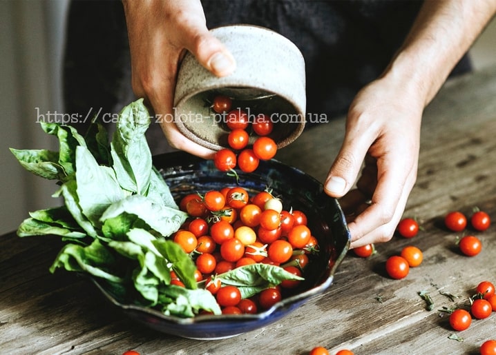 Hands pouring cherry tomatoes from a bowl into a dish of fresh basil leaves