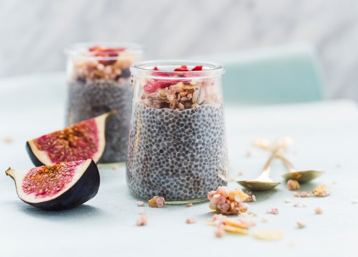 Two chia pudding parfaits topped with fig and granola on blue linen