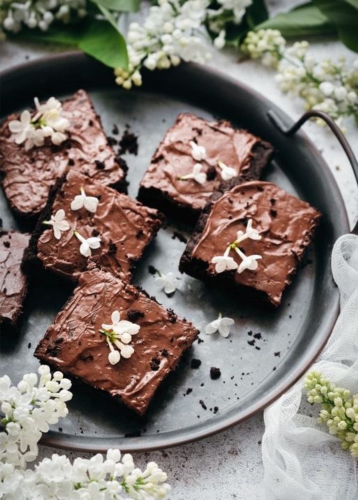 Schokoladen-Brownie-Stücke mit weißen Fliederblüten auf einem dunklen Teller