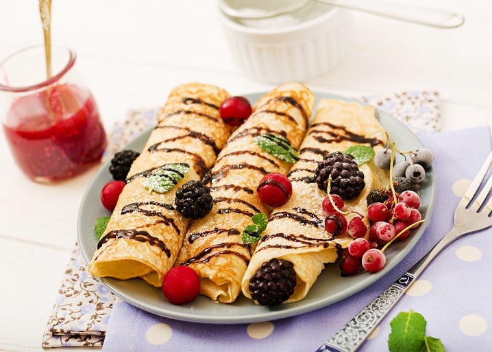 Млинці-рулетики политі шоколадом з вишнями, ожиною, порічками та чорницею на сірій тарілці