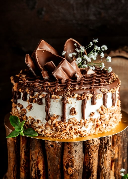 Chocolate drip layer cake with nut crumble and chocolate shards on a wood stand
