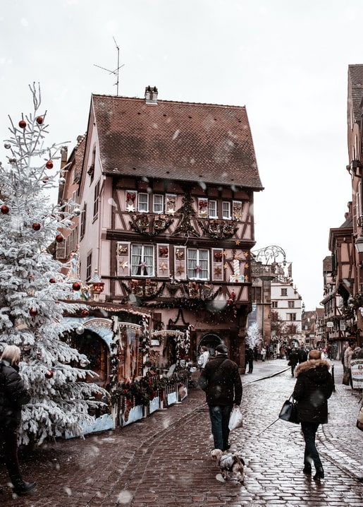 Verschneites Fachwerkhaus weihnachtlich geschmückt, mit Baum und Passanten mit Hund auf Kopfsteinpflaster