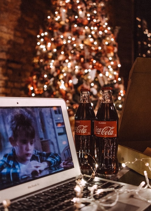Laptop zeigt Weihnachtsfilm neben zwei Cola-Flaschen aus Glas und einer Lichterkette