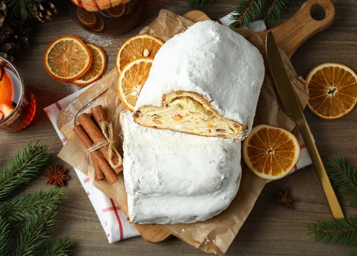 Aufgeschnittener Stollen mit Puderzucker neben getrockneten Orangenscheiben und Zimtstangen