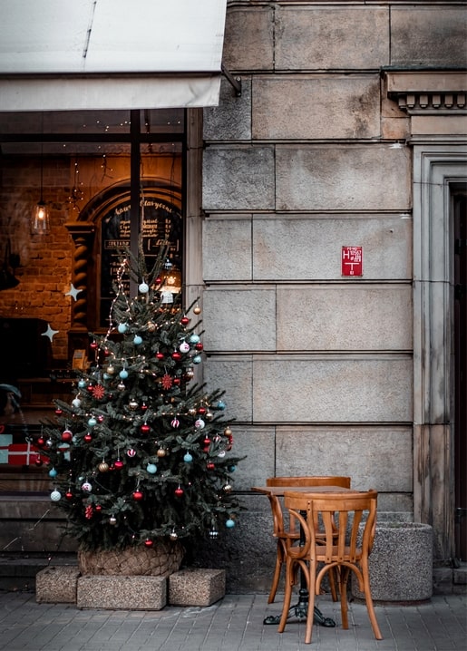 Small decorated Christmas tree beside empty wooden café chairs on a city street corner