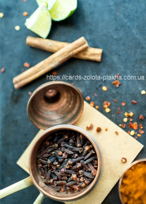 Cinnamon sticks and cloves in a copper bowl with lime wedges and chili flakes