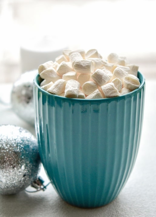 Türkisfarbener Rillenbecher mit Marshmallows neben silbernen Weihnachtskugeln