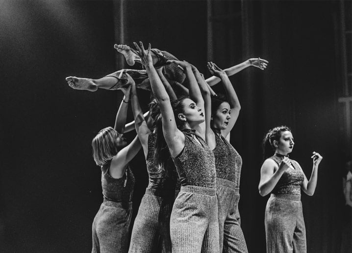 Schwarzweißfoto tanzender Frauen, die die Beine einer Partnerin in dramatischer Gruppenpose heben