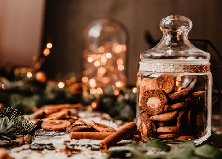 Glas mit Lebkuchen, Zimtstangen und einer verschwommenen Lichterkette im Hintergrund