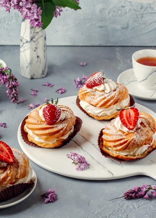 Cream puff pastries with strawberries beside a teacup and lilac blossoms