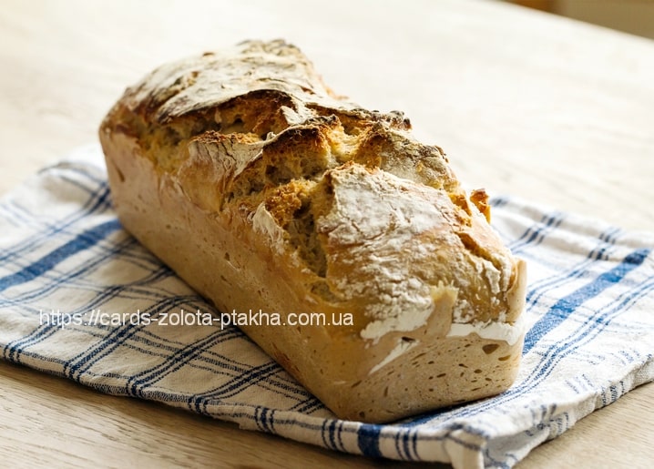 Knuspriger goldener Brotlaib auf kariertem Geschirrtuch, mit Mehl bestäubt, auf einem Holztisch.