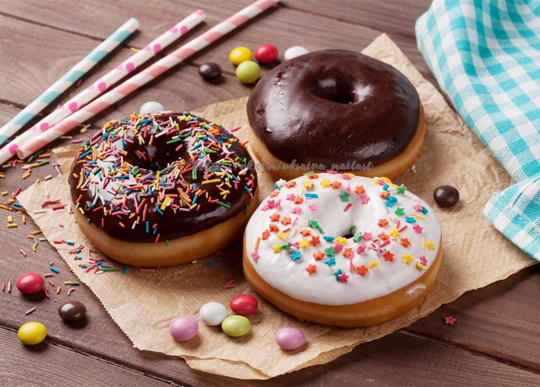 Drei glasierte Donuts mit Streuseln, Schokolade und Bonbons auf einem Holztisch