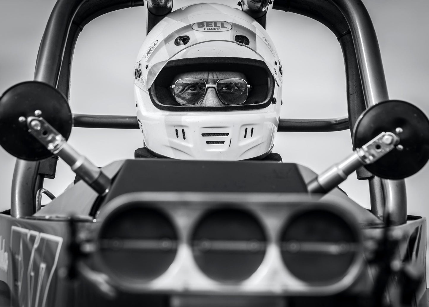 Schwarzweißaufnahme eines Dragster-Fahrers mit Helm und Sonnenbrille hinter dem Steuer