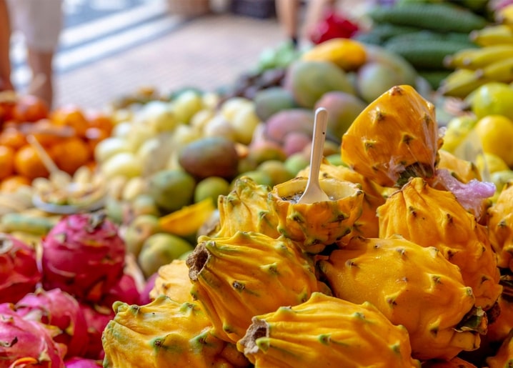 Haufen gelber Drachenfrüchte mit Löffel auf einem tropischen Marktstand