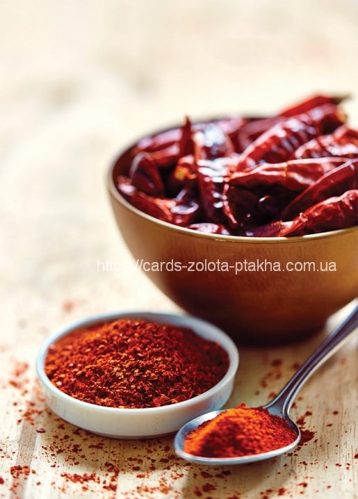 Copper bowl of dried red chili peppers next to a spoonful of ground paprika
