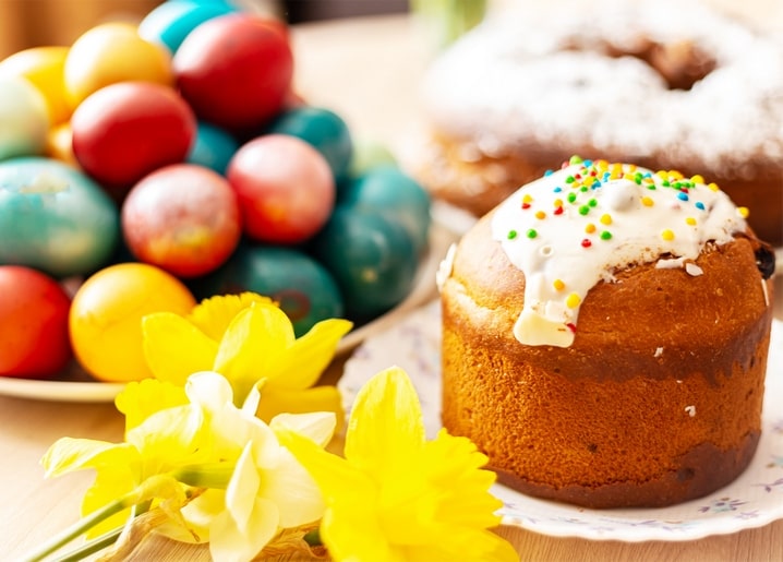 Pyramid of red, teal, and gold dyed Easter eggs beside a paska cake and yellow daffodils