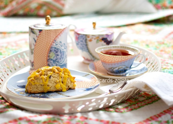 Geblümte Teekanne, Tasse Tee und zitronenglasierter Scone auf Patchwork-Decke