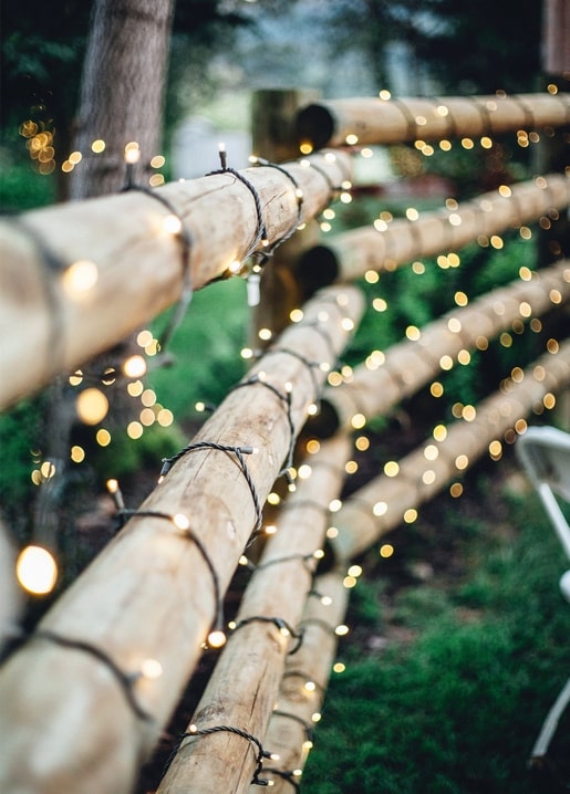 Warm fairy lights wound around wooden posts in a garden at dusk