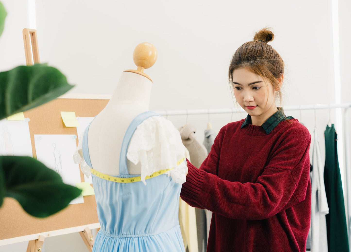 Junge Modedesignerin misst ein blaues, spitzenbesetztes Kleid an einer Schneiderpuppe im Atelier.