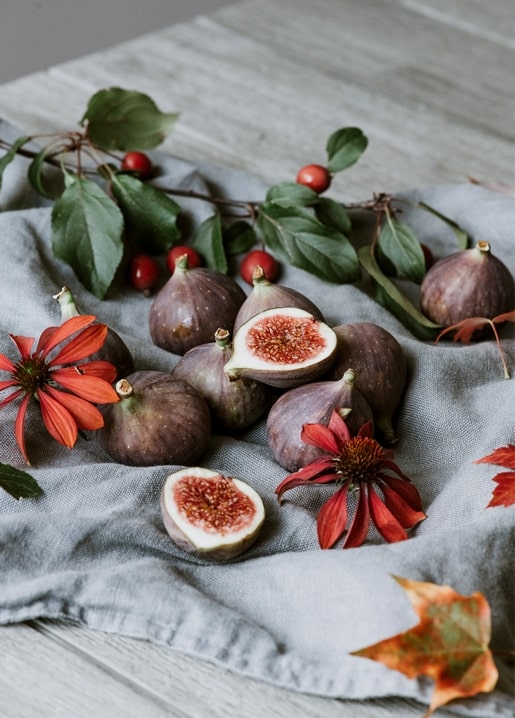Aufgeschnittene Feigen, Hagebutten und orangefarbene Blüten auf Leinen