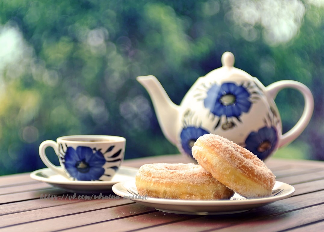 Blau-weiße Blumen-Teekanne mit Tasse neben zwei gezuckerten Donuts im Garten