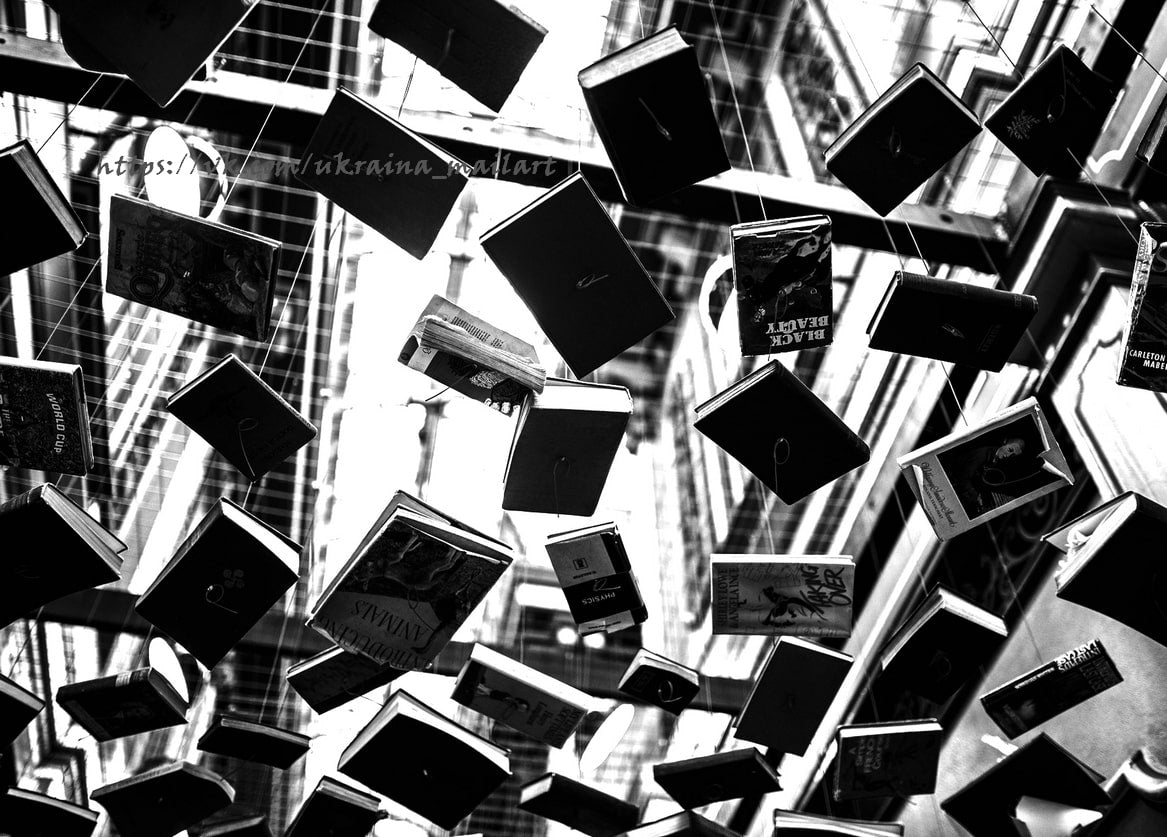 Schwarz-weißes Foto von Hunderten Büchern, die an Fäden über einem Treppenhaus schweben