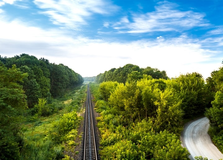 Straight railway track through a green summer forest under blue sky