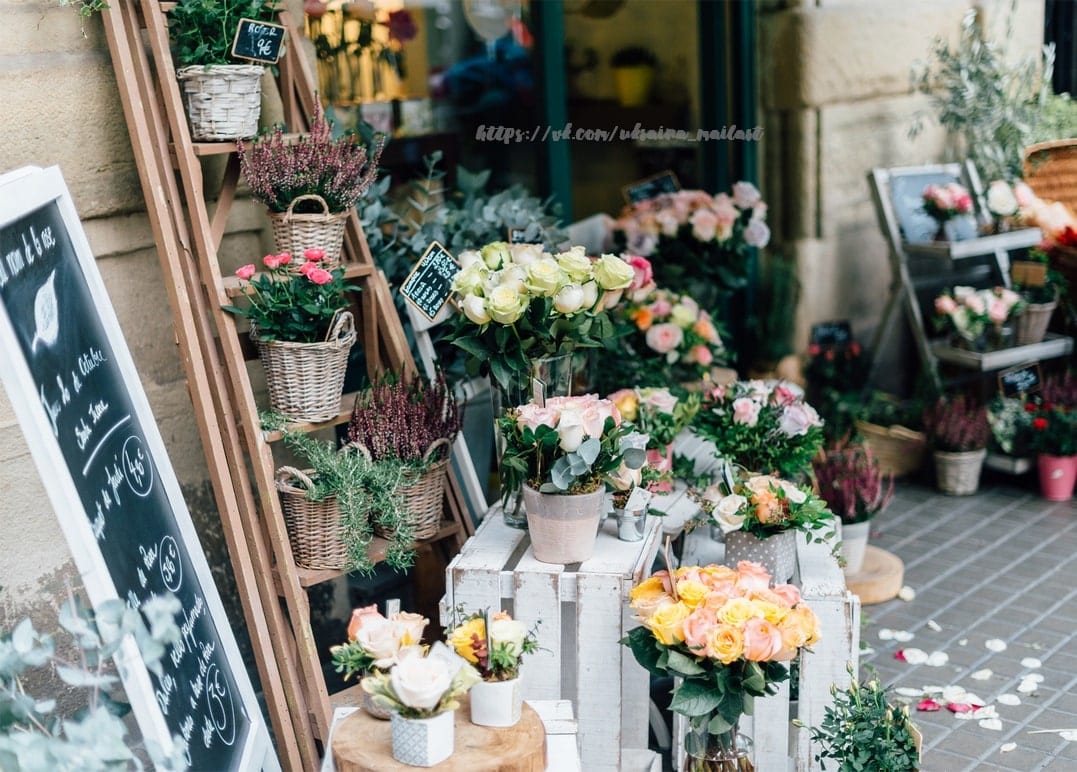 Weidenkörbe mit Rosen und Heidekraut vor einem französischen Blumenladen an einer Kopfsteinpflasterecke
